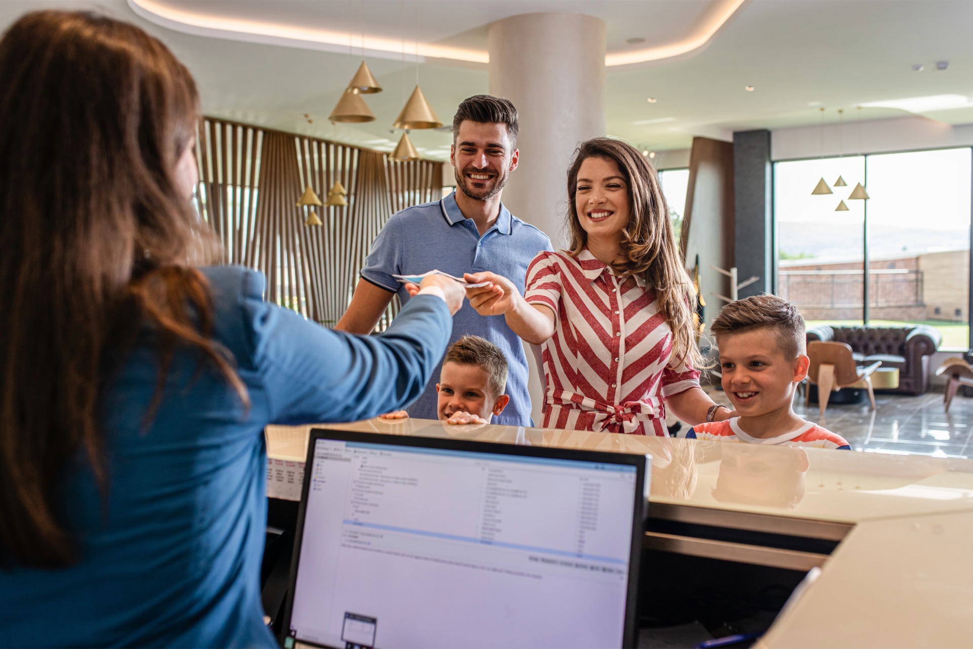 a smiling family of four is greeted at a hotel service desk