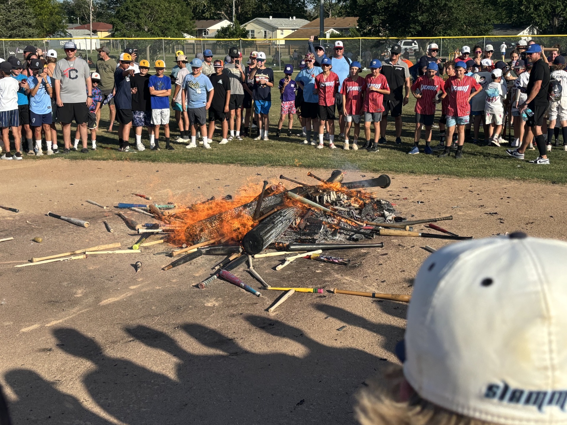 A pile of wooden baseball bats burns as observers smile