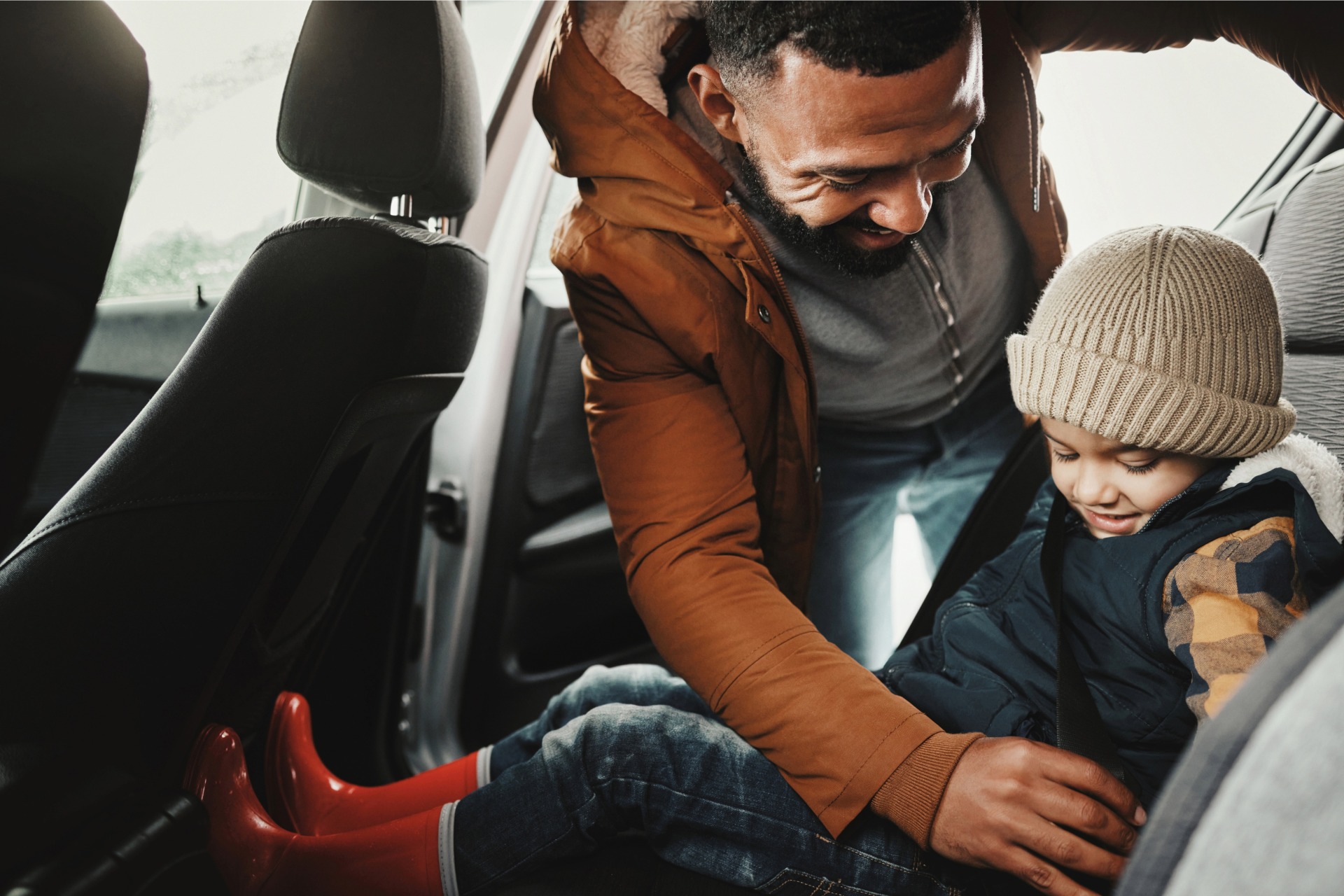 An adult reaches into the rear seat to buckle a child wearing winter cap