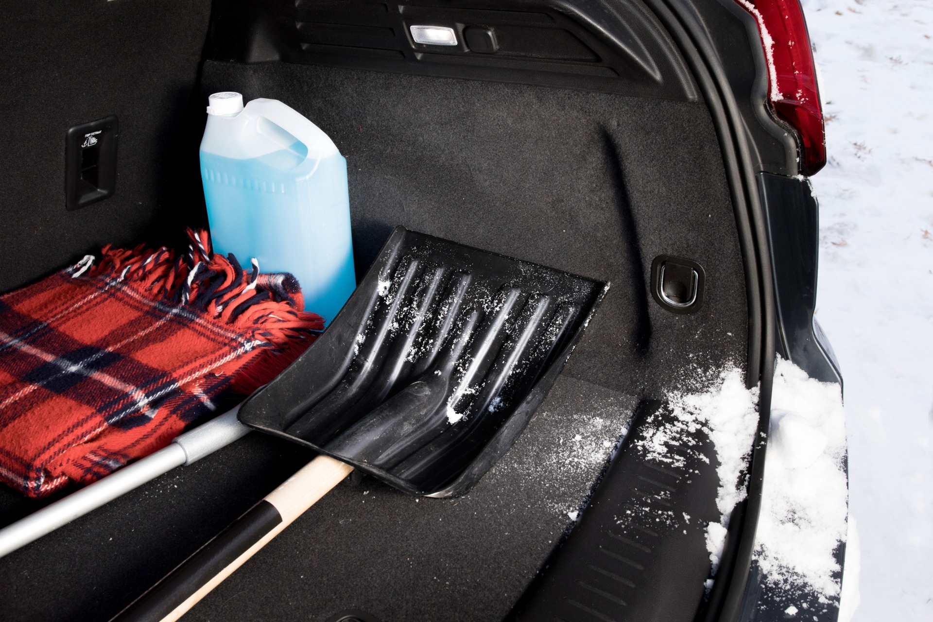 A blanket, shovel, and wiper fluid sit in the trunk of a vehicle